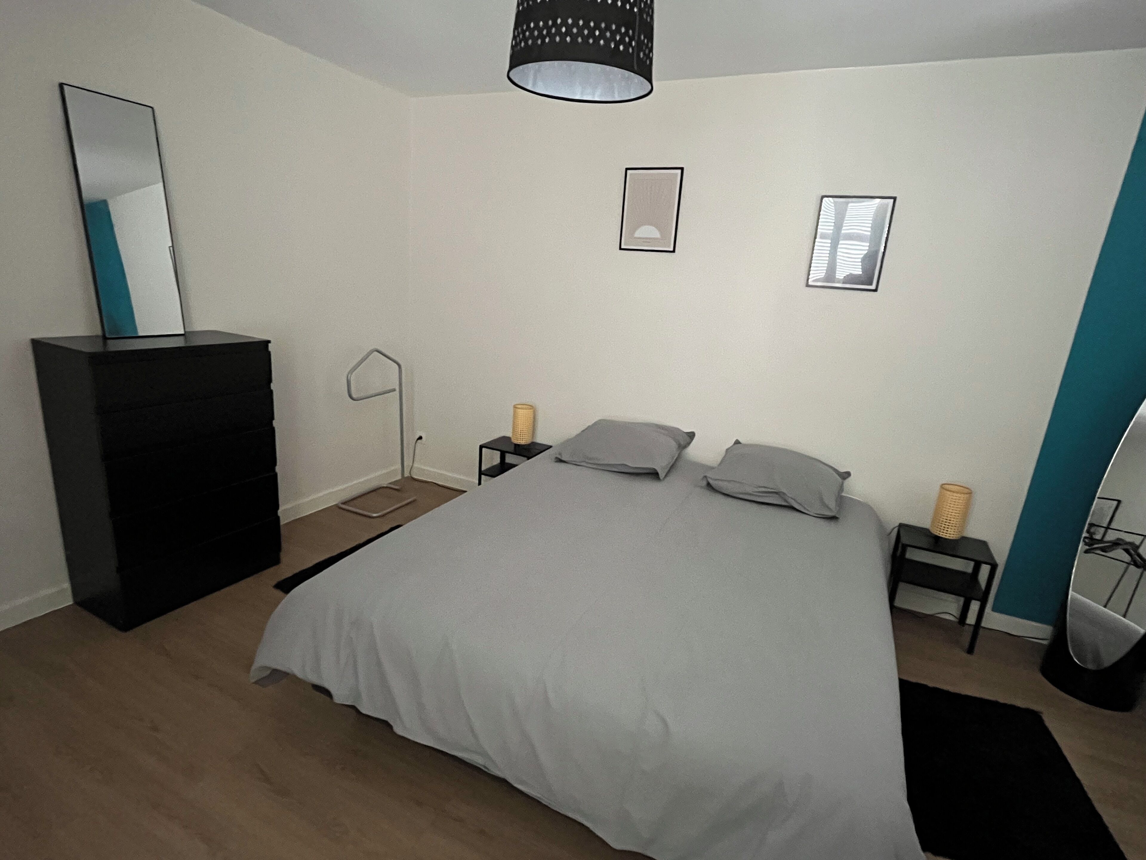 Un dormitorio con cama, cómoda, mesita de noche, lámpara y espejo.