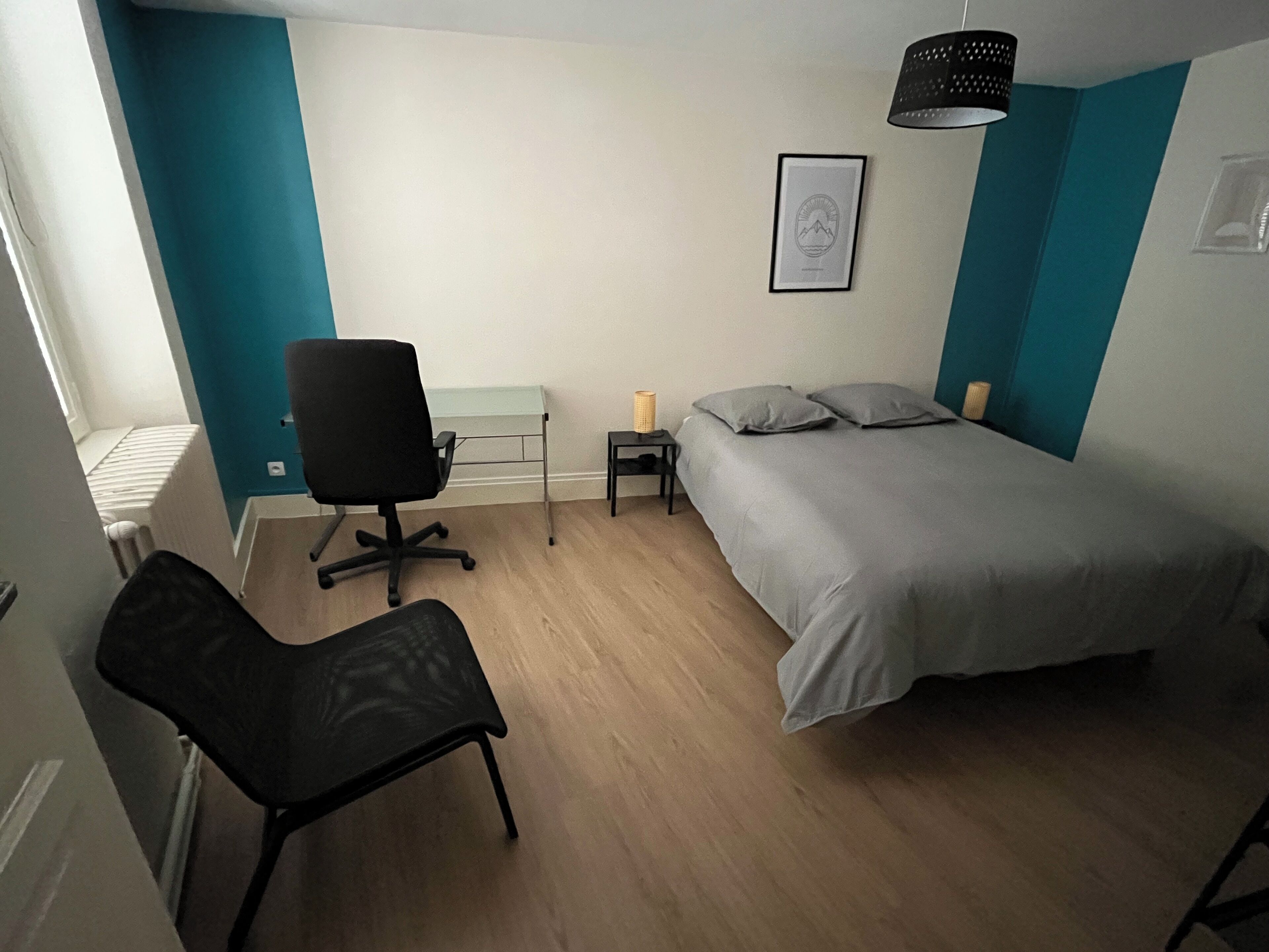 A bedroom with a bed, a desk, a chair, and a small table.
