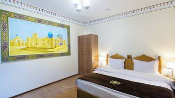 A hotel room with a large painting of a historical building, a wooden wardrobe, a bed with white and brown bedding, and a chandelier.