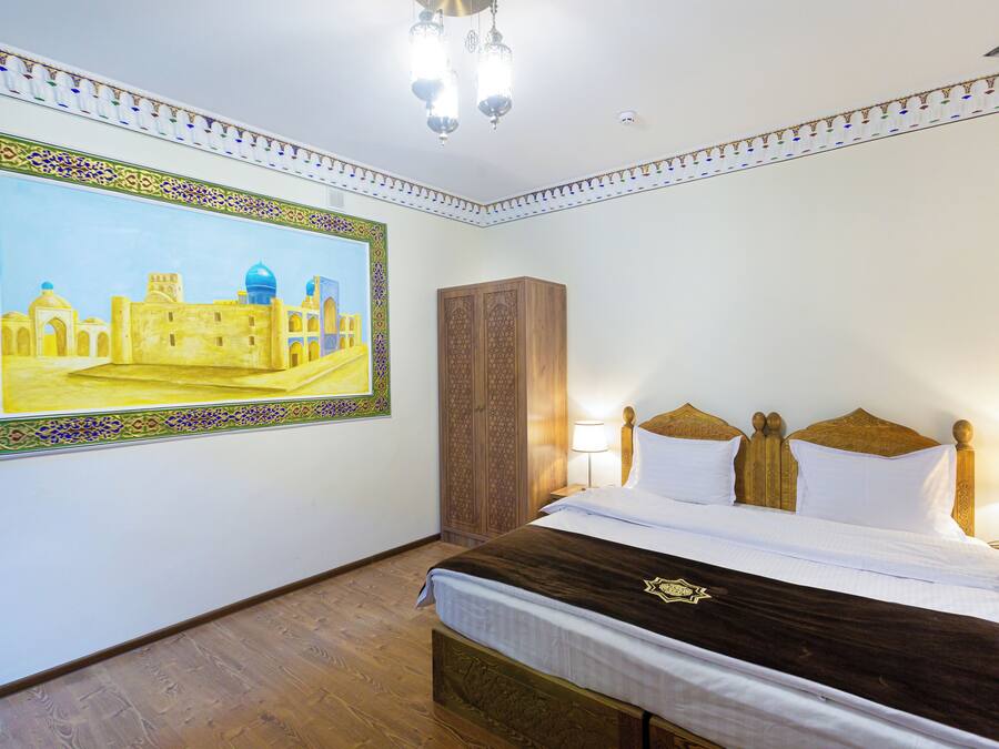 A hotel room with a large painting of a historical building, a wooden wardrobe, a bed with white and brown bedding, and a chandelier.