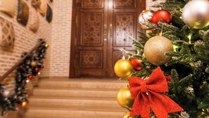 A Christmas tree with ornaments and a red bow, a staircase, and a wooden door in the background. - Hotel Iman (Bukhara)