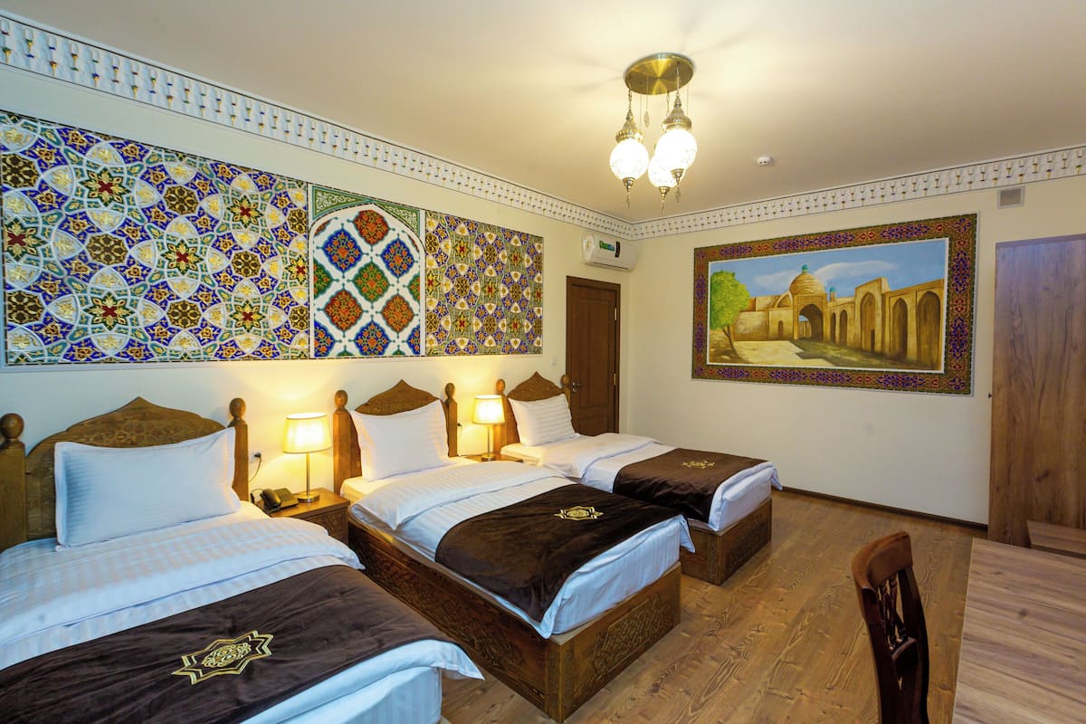 Habitación de hotel con dos camas, piso de madera, un cuadro de una mezquita y un detalle decorativo en la pared.