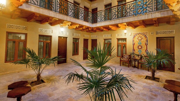 A spacious atrium with high ceilings, wooden beams, and a central open area with potted plants. - Hotel Iman (Bukhara)