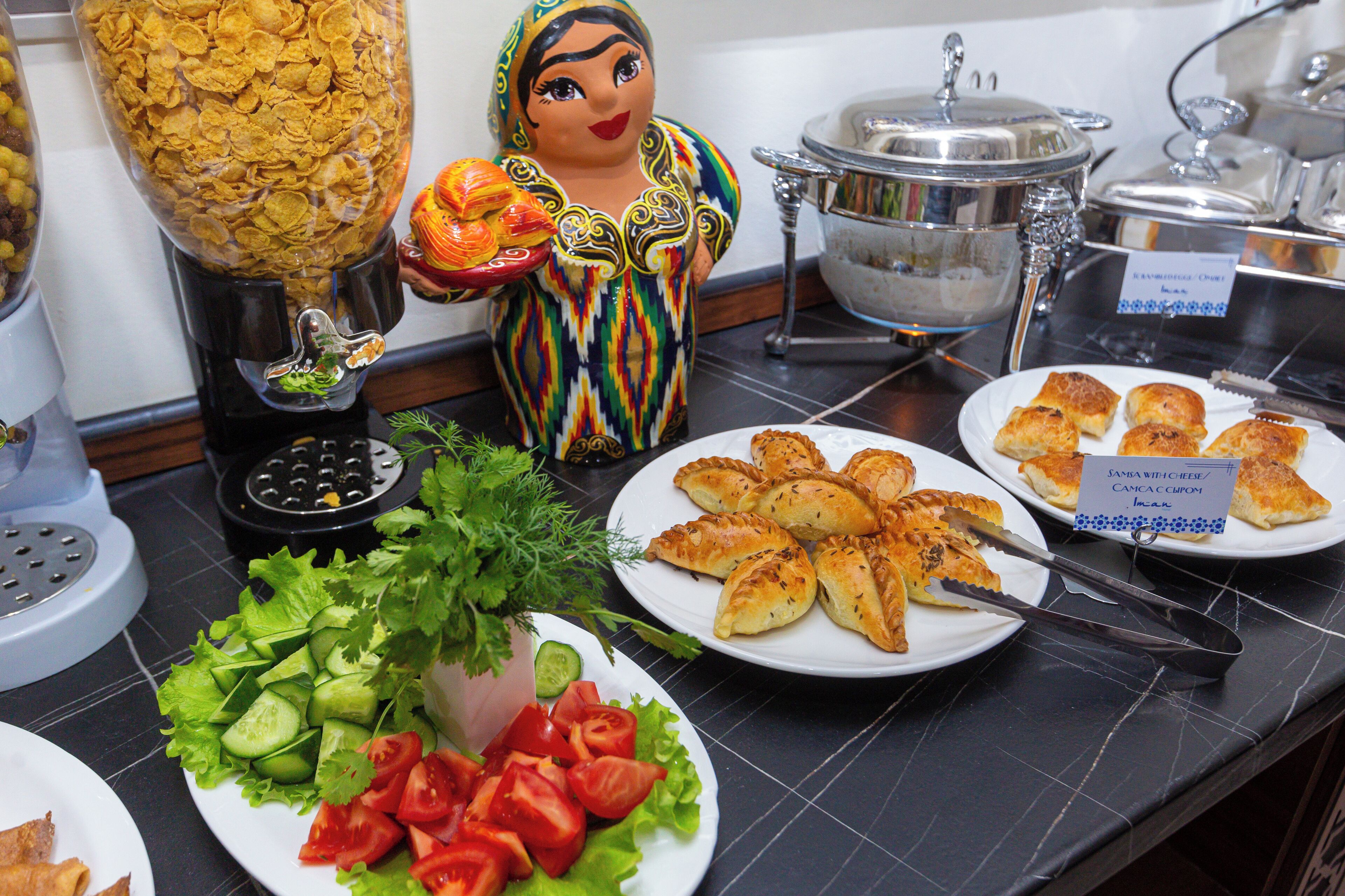 Una mesa de buffet con diferentes opciones de comida, como ensaladas, pasteles y un recipiente grande de cereales.