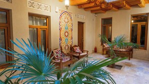 A spacious lobby with wooden furniture, a decorative wall hanging, and potted plants. - Hotel Iman (Bukhara)