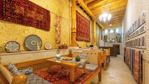 A traditional interior with a wooden bench, a table, and a sofa with patterned cushions. - Hotel Iman (Bukhara)