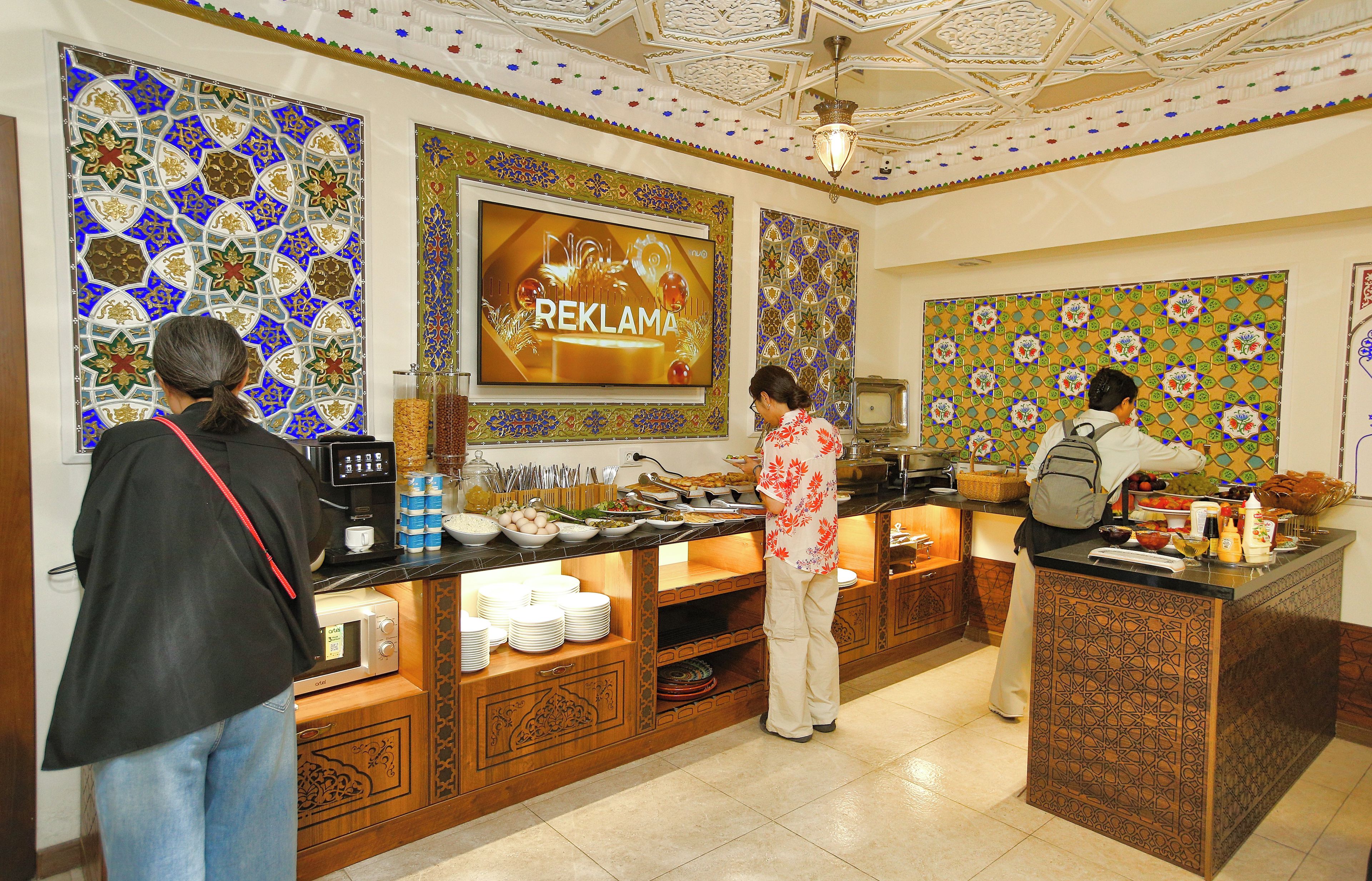 Zona de buffet con diversas opciones de comida y una pantalla mostrando 'REKLAMA'.