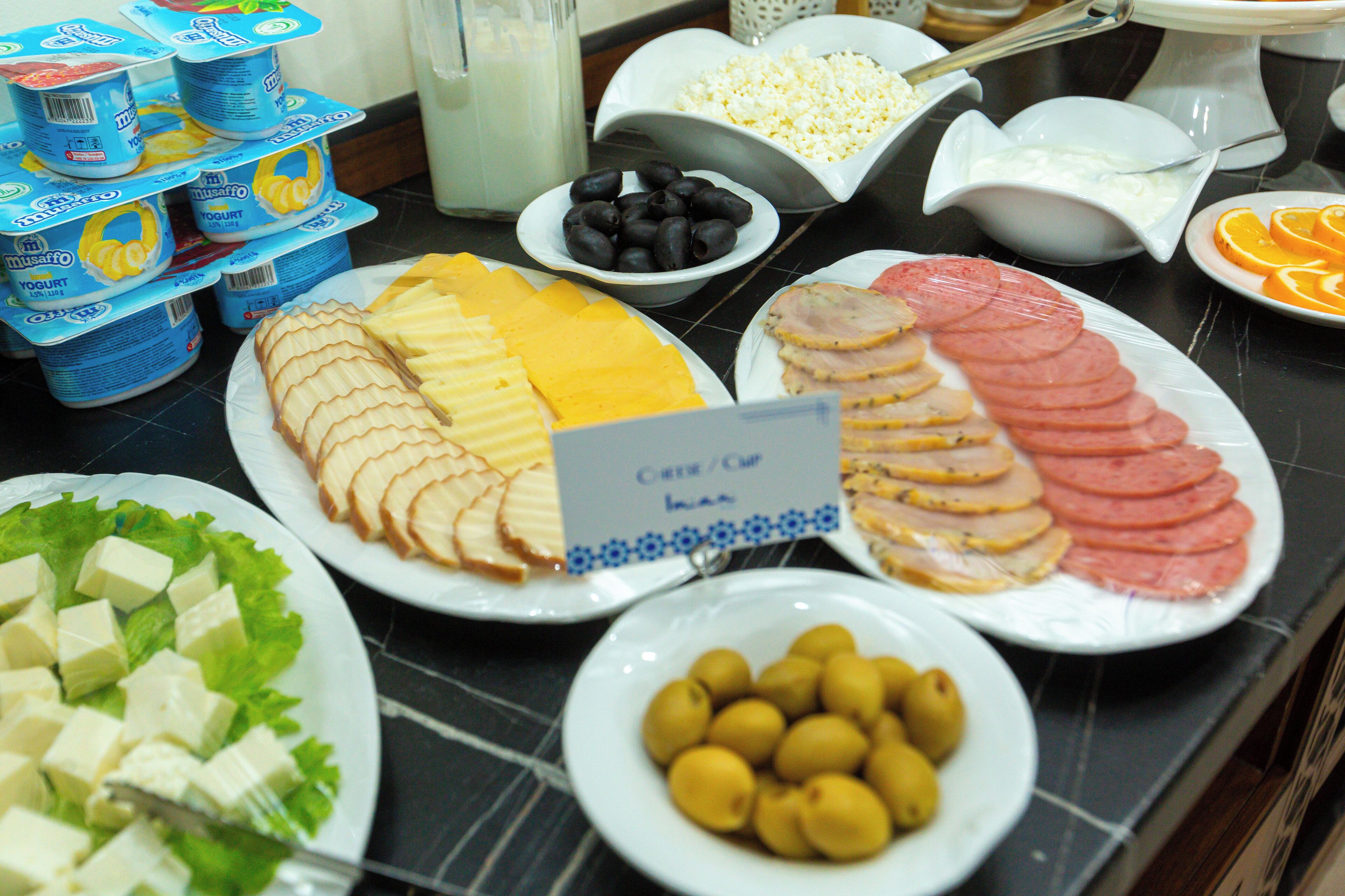 Un bufé con diversos alimentos, como queso, jamón, aceitunas y yogur.