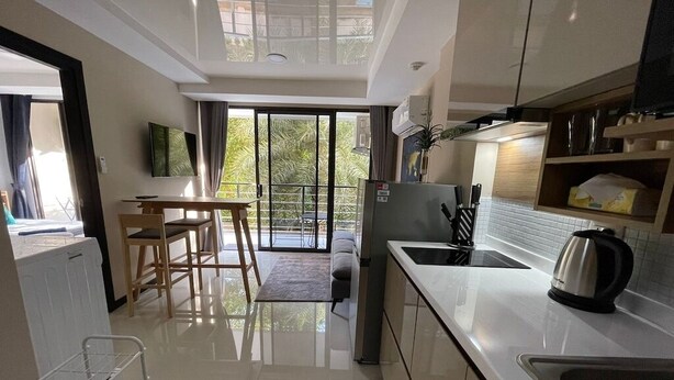 A modern kitchen with a large island, a dining area with a table and chairs, and a view of greenery through the sliding glass doors. - Cosy 1-bedroom apartment in a pleasant walking location to Yanui beach  (Tambon Rawai)