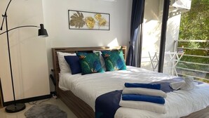A neatly made bed with blue and white bedding, a grey furry rug, a floor lamp, and a wall with a leaf-patterned artwork. - Cosy 1-bedroom apartment in a pleasant walking location to Yanui beach  (Tambon Rawai)