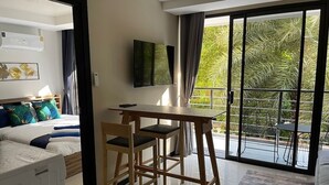 A modern hotel room with a bed, a desk, and a view of a pool and greenery. - Cosy 1-bedroom apartment in a pleasant walking location to Yanui beach  (Tambon Rawai)