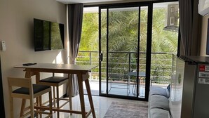 A modern living room with a sofa, a dining table with chairs, a flat-screen TV, and a sliding glass door leading to a balcony with outdoor furniture. - Cosy 1-bedroom apartment in a pleasant walking location to Yanui beach  (Tambon Rawai)