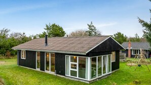 Une maison moderne avec une grande façade vitrée, un toit foncé et une pelouse bien entretenue.