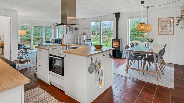 Une cuisine moderne dotée d’un îlot central, d’un four encastré et d’une cuisinière. On y trouve également un coin repas avec une table et des chaises, ainsi qu’une grande fenêtre offrant une vue sur l’extérieur.