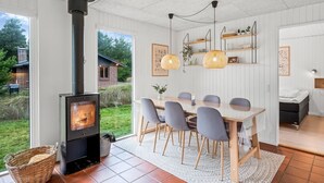 Une pièce chaleureuse avec un poêle à bois, une table à manger avec des chaises et une vue sur l’extérieur.