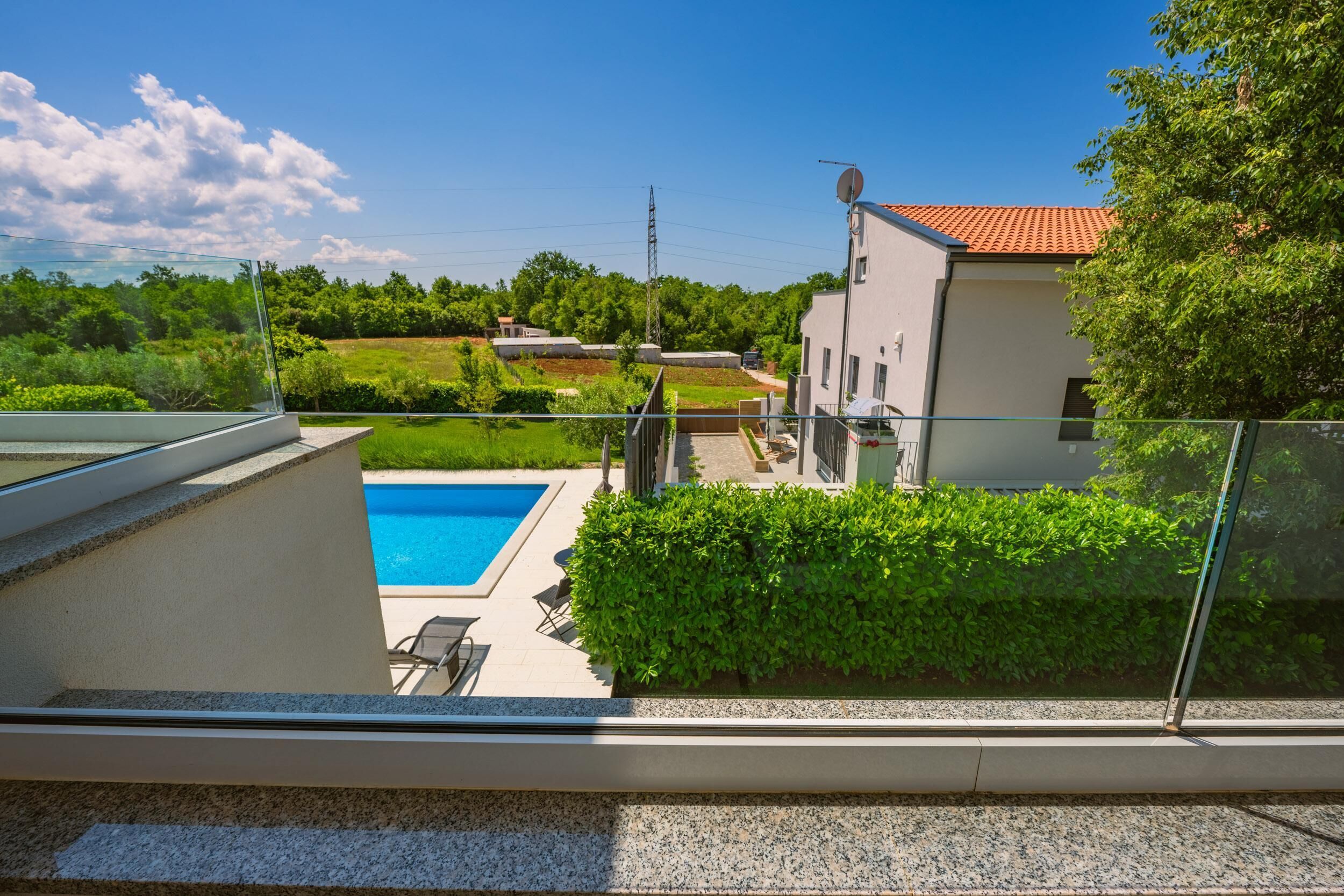 Il s’agit d’une propriété résidentielle dotée d’une piscine, d’une balustrade en verre et offrant une vue sur la verdure environnante et les bâtiments situés au loin.