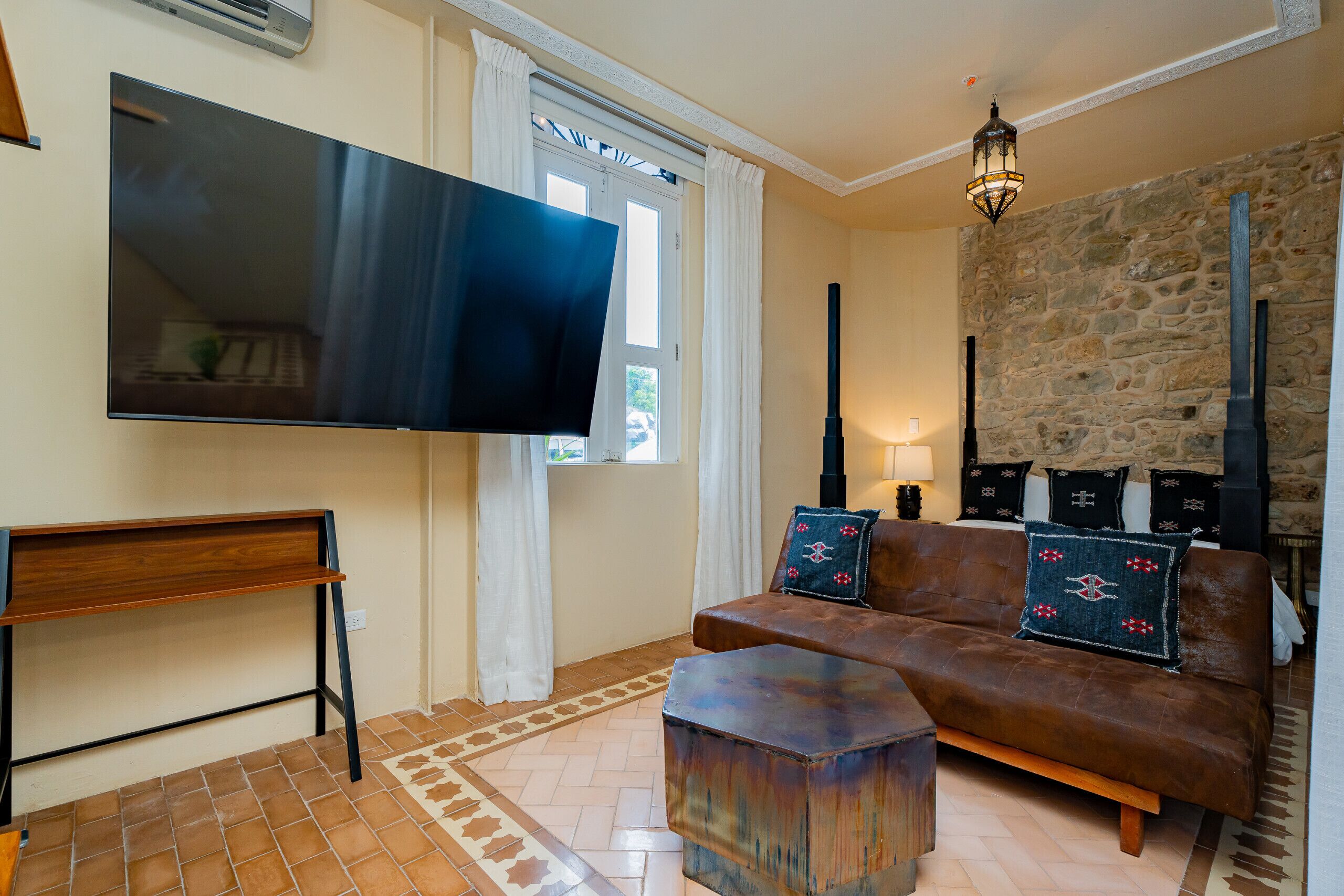 Un salon doté d’un téléviseur à écran plat, d’un canapé en cuir marron, d’une table basse en bois, d’un mur en pierre et d’un tapis à motifs.