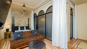 A room with a brown sofa, a small wooden table, a stone wall, a bed with black headboard, and a large window with white curtains. - Room deluxe with communal pool Ma4 (Ciudad de Panamá)