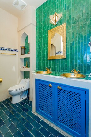 Ein Badezimmer mit grüner Fliesenwand, einer weißen Toilette und einem blauen Waschtischschrank.