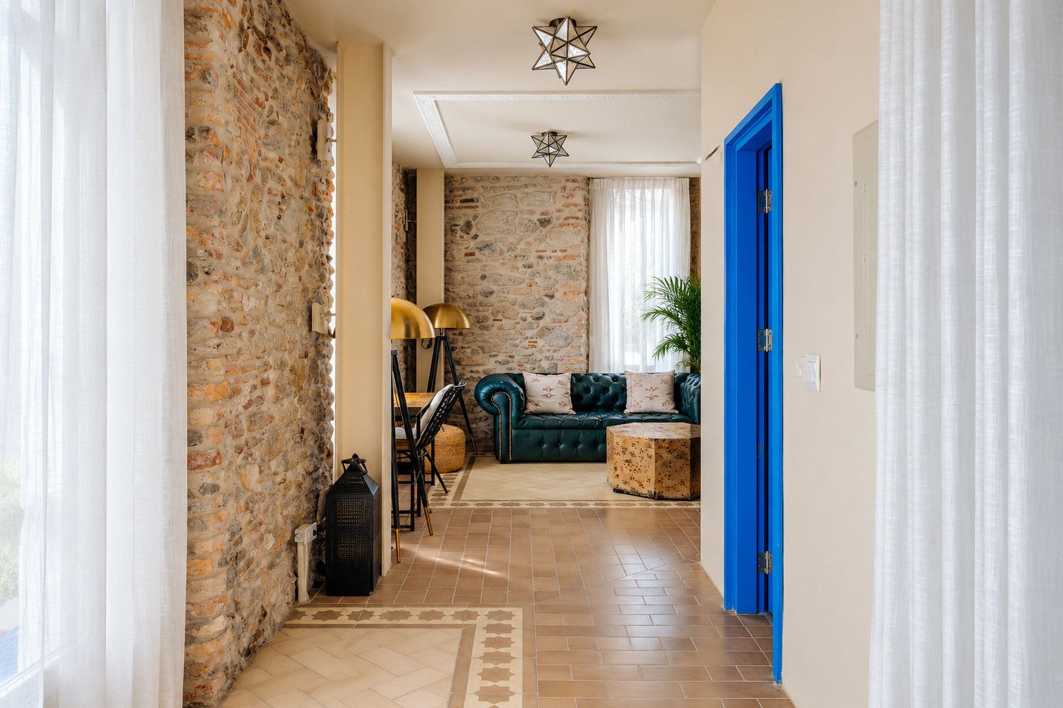 Un pasillo con pared de piedra, una puerta azul, un sofá verde y una alfombra estampada.
