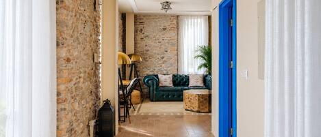 Un pasillo con pared de piedra, una puerta azul, un sofá verde y una alfombra estampada.
