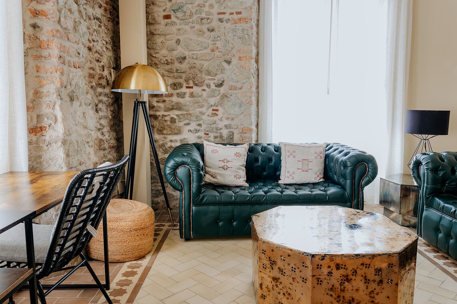 A cozy room with a stone wall, a green leather sofa, a round coffee table, and a lamp.