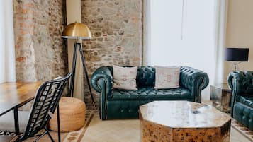 A cozy room with a stone wall, a green leather sofa, a round coffee table, and a lamp.