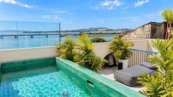 A rooftop swimming pool with a view of a body of water and distant hills.