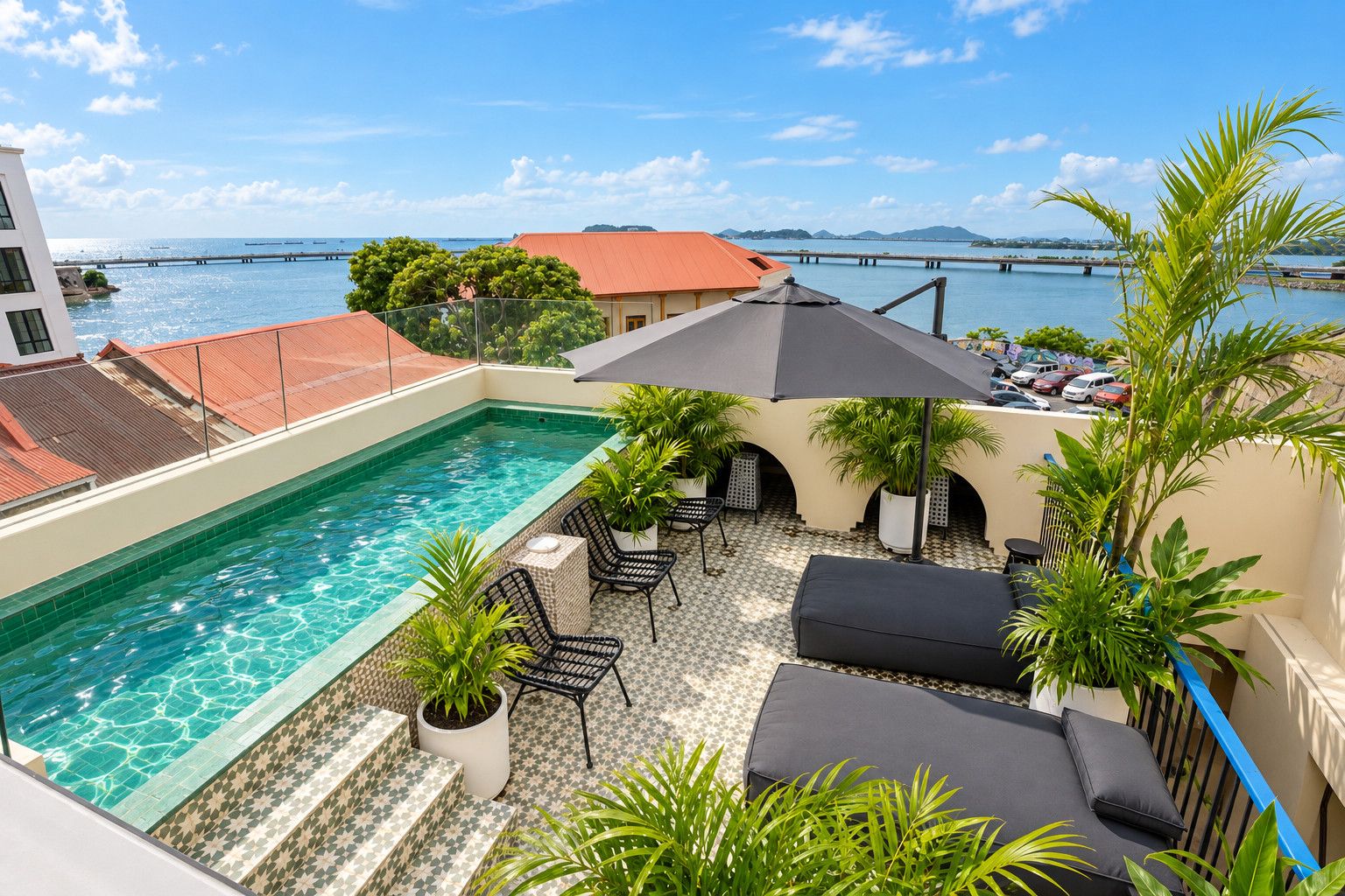 Une piscine sur le toit avec vue sur la mer, des espaces de détente en plein air et un pont en arrière-plan.