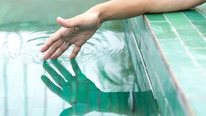 Eine Hand greift ins Schwimmbecken, im Hintergrund steht ein Getränk.