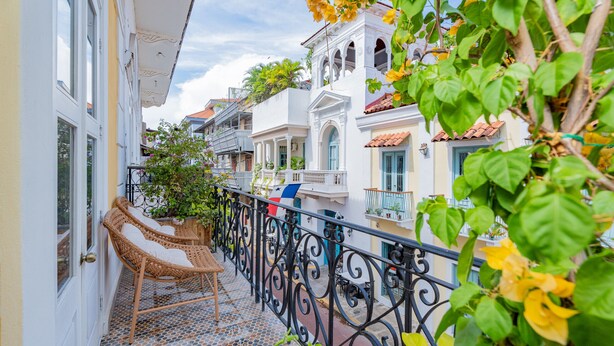 Ein Balkon mit Korbstühlen, Fliesenboden und schmiedeeisernem Geländer.
