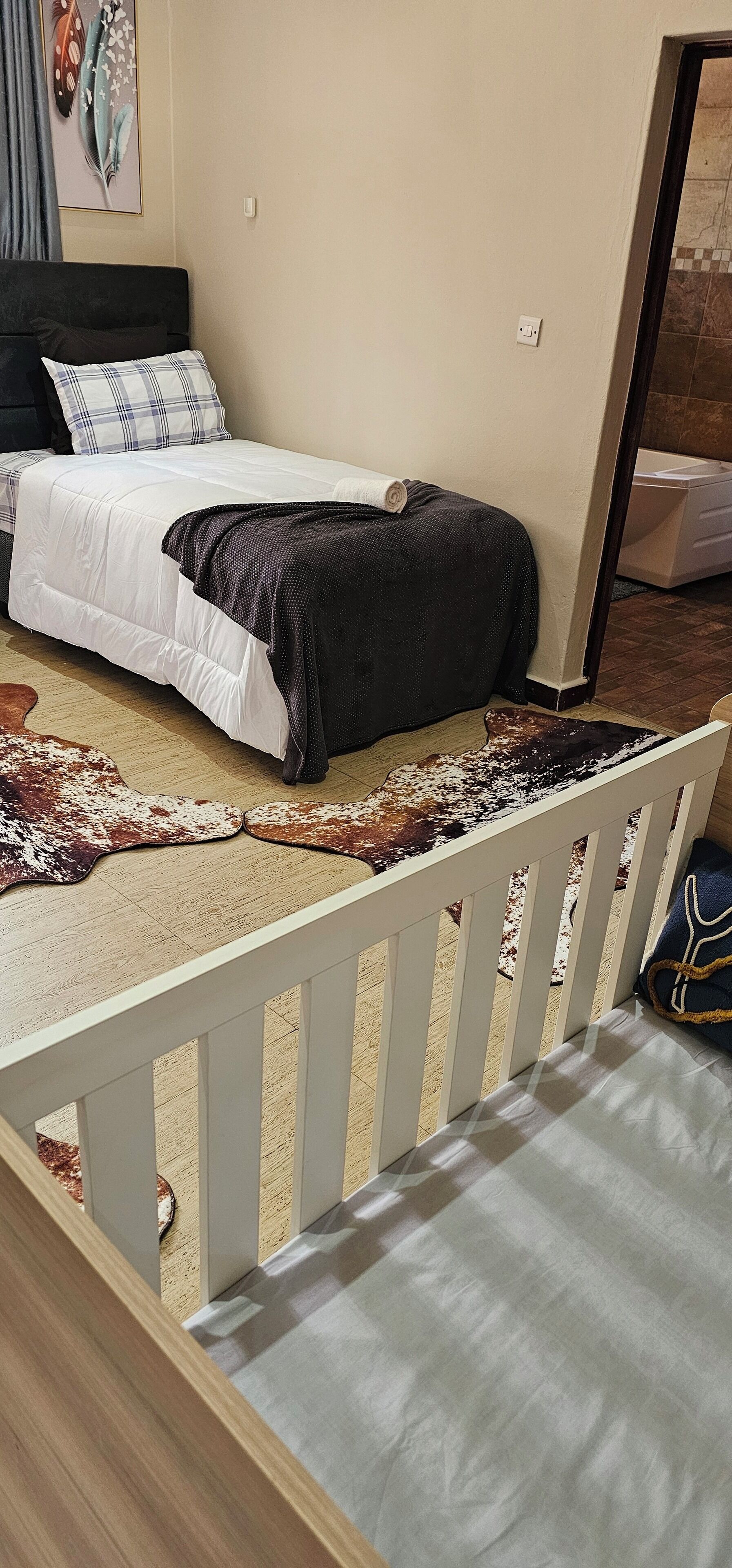 A bedroom with a bed, a white headboard, a dark blanket, and a patterned rug.