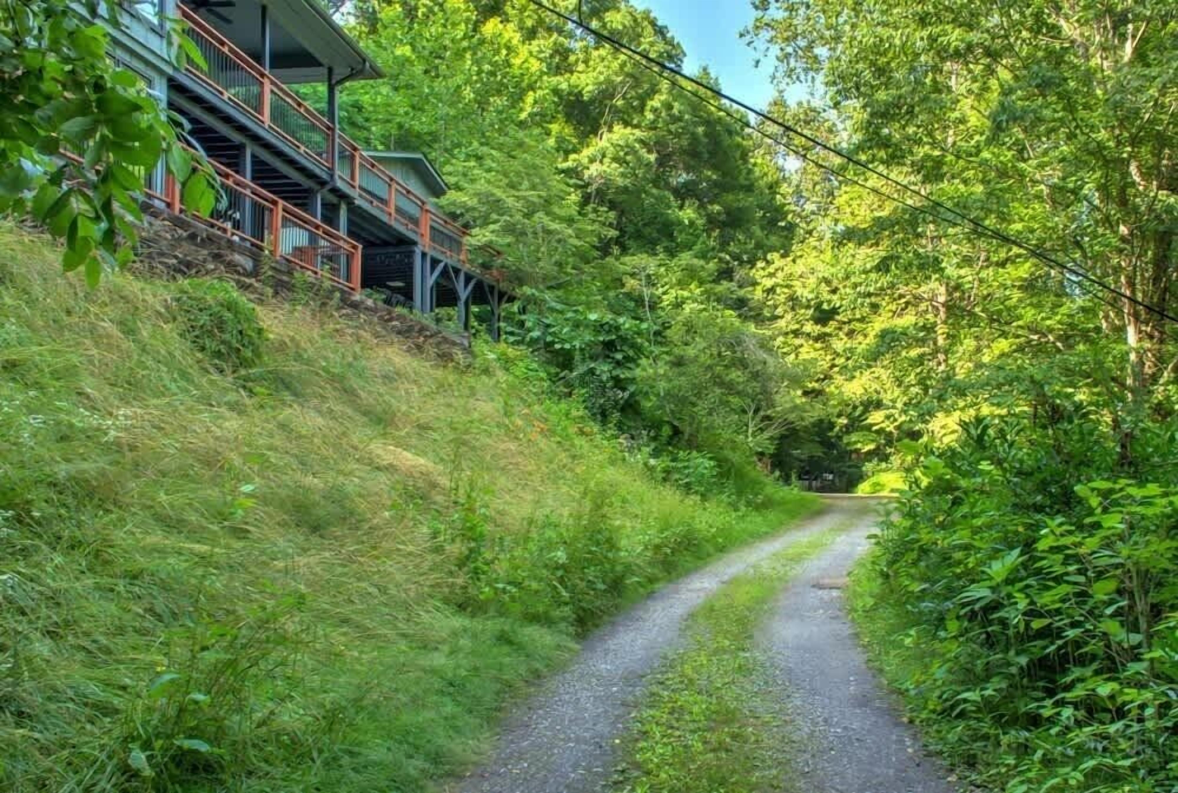 A gravel path leading through a forested area with a building featuring a staircase and a covered walkway.