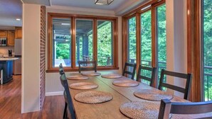 Comedor con una mesa larga, varias sillas y grandes ventanales que ofrecen vistas a la vegetación.