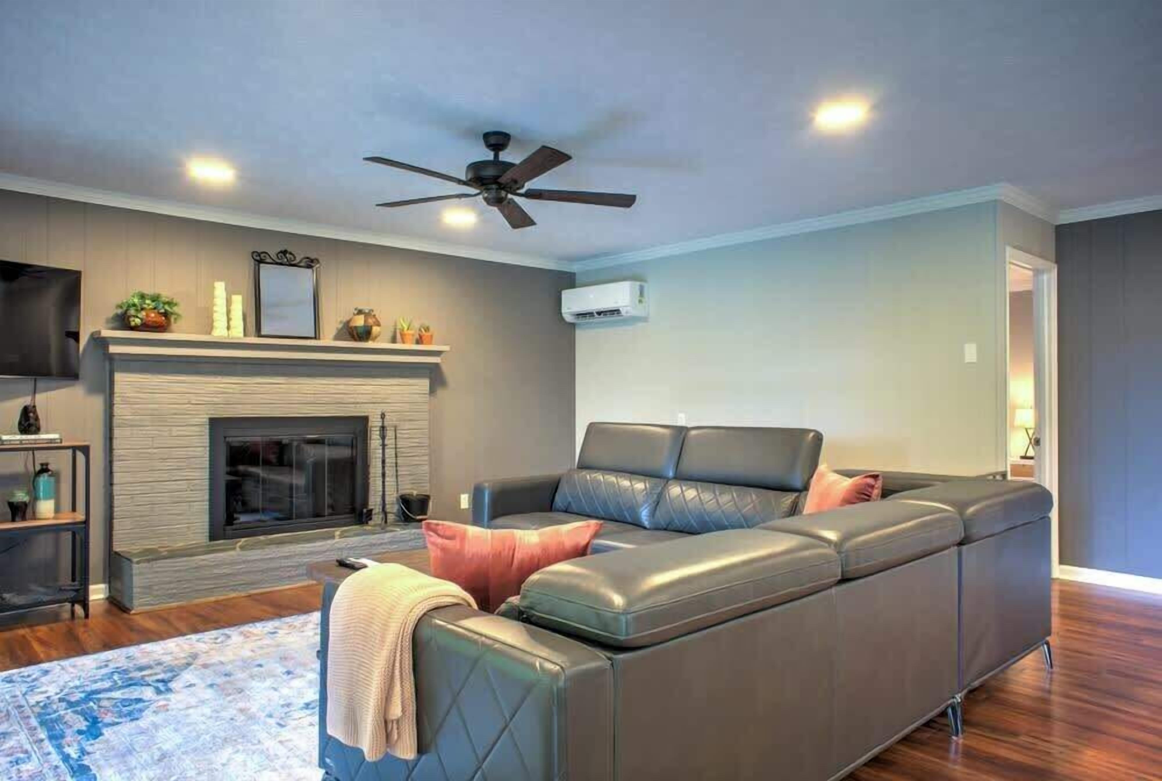 A living room with a sectional sofa, a fireplace, a ceiling fan, and a television.