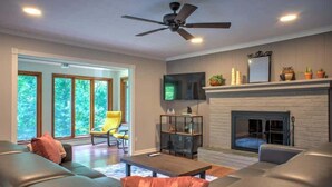 Una sala de estar moderna con chimenea, sofás de cuero, un televisor y un ventilador de techo.