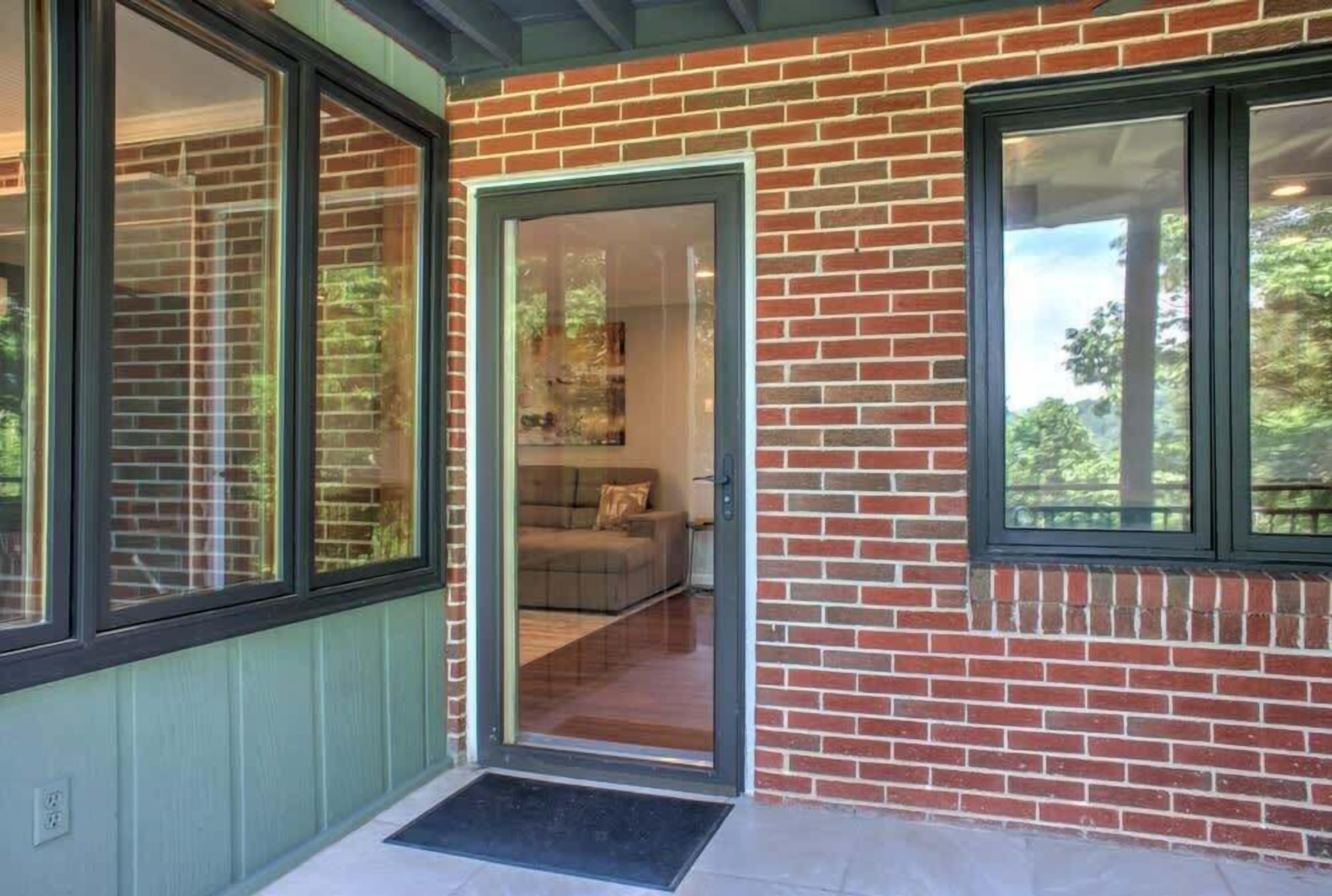 A brick exterior with a glass door leading to a living area with a sofa and cushions.