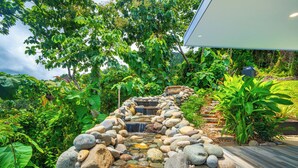 Een tuin met een waterornament van steen, weelderige beplanting en een houten terras.