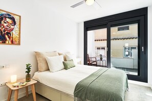 Une chambre à coucher moderne avec un lit, une petite table de chevet, un plaid vert et un tableau accroché au mur.