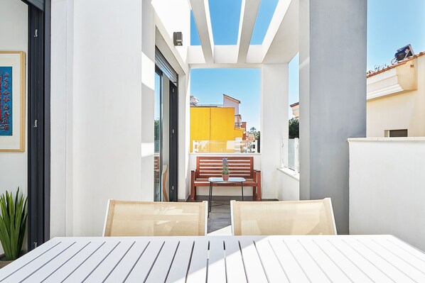 Un balcon avec une table et des chaises, un banc et un pot de fleurs.