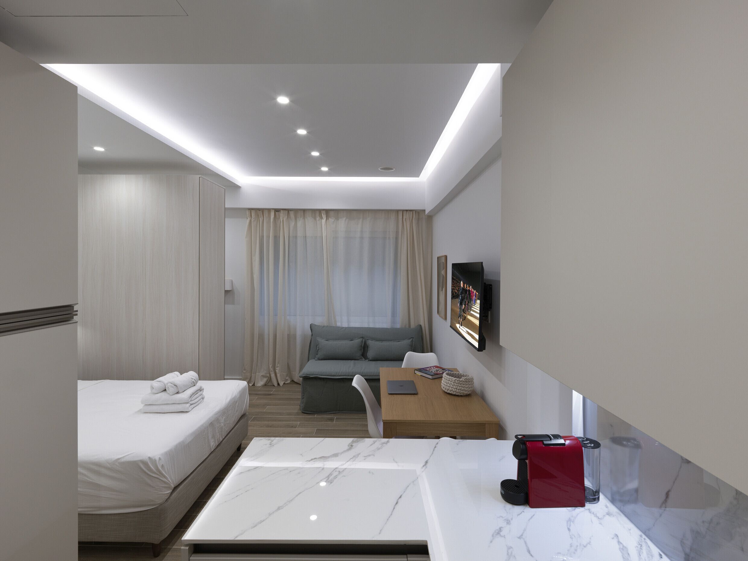 A modern hotel room with a bed, a sofa, a desk, and a coffee machine.
