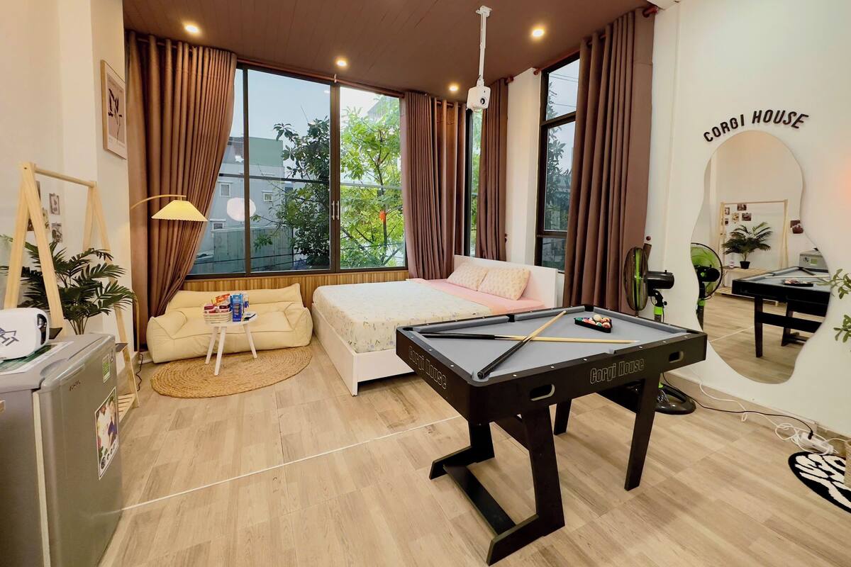 Ein Schlafzimmer mit Bett, Billardtisch, Schreibtisch und großem Fenster mit Vorhängen.