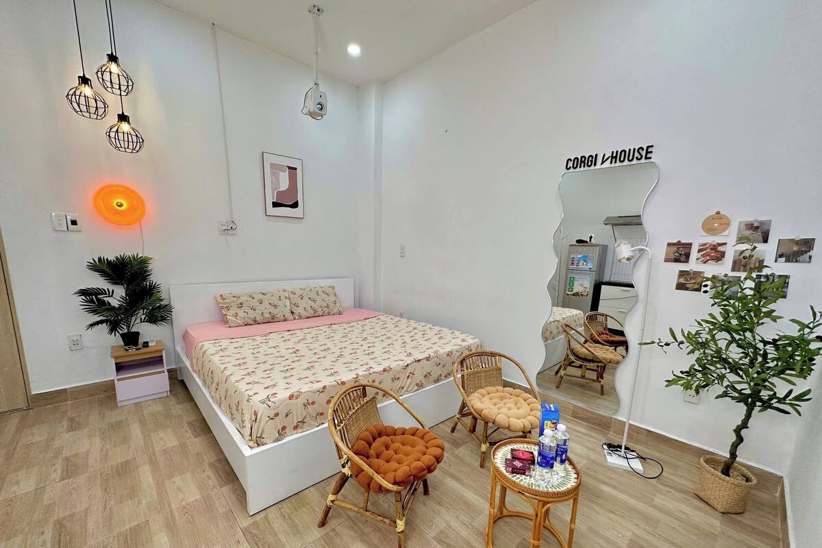 Ein Schlafzimmer mit einem Bett, zwei Korbstühlen, einem kleinen Tisch, einer Topfpflanze und einem an der Wand befestigten Spiegel.