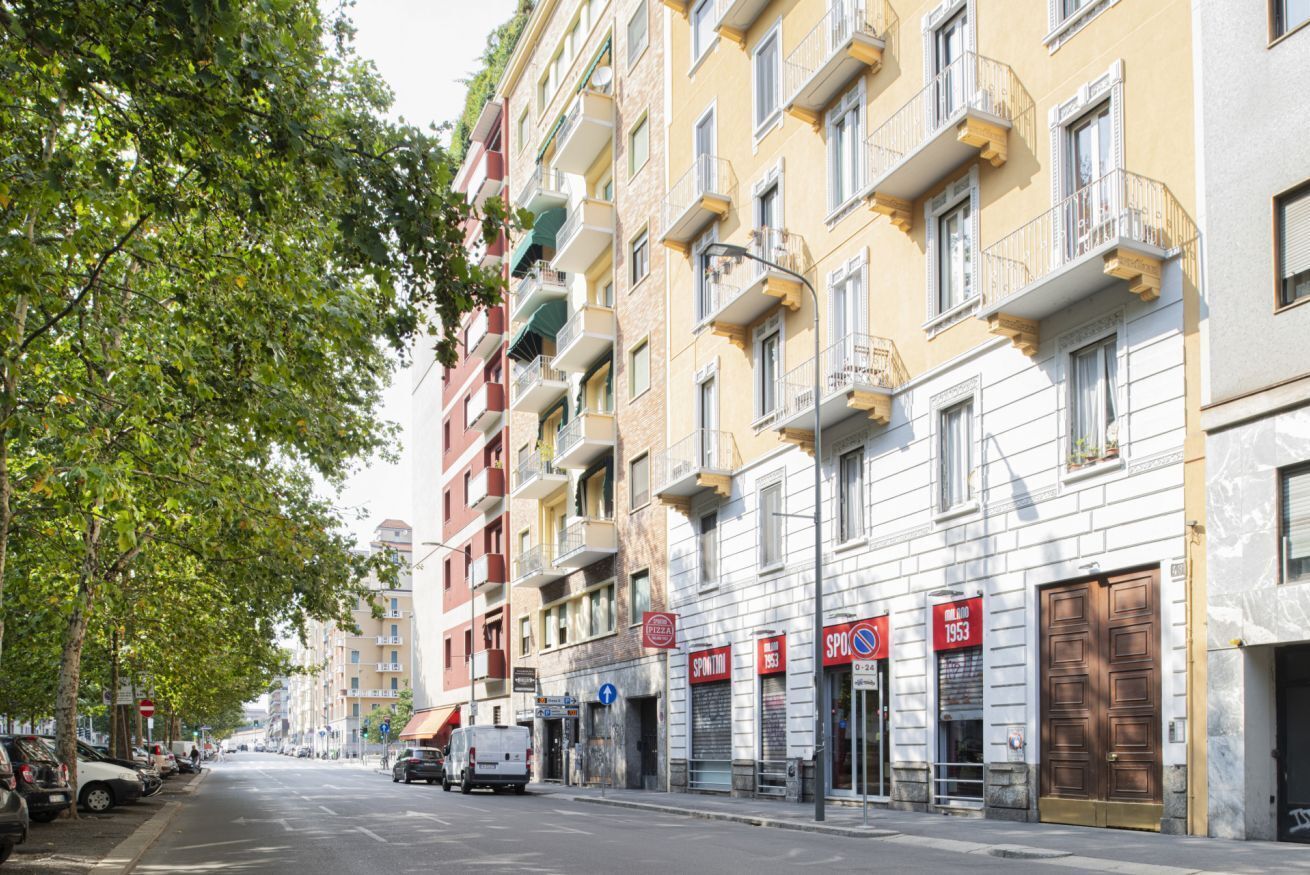 Vista da rua com edifícios altos, carros estacionados e céu claro.