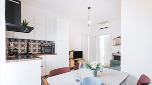 A modern kitchen with white cabinets, a microwave, and a black range hood. There is a dining table with blue plates and a vase of flowers. - Easylife - Apartment with balcony near Navigli (Milano)