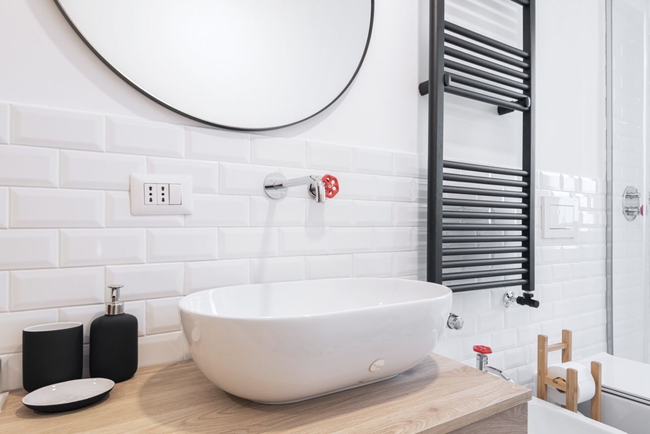 A modern bathroom with a large white bathtub, a round mirror, and a towel rack.