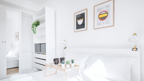 A minimalist bedroom with a bed, a bedside table with decorative items, a wardrobe, and a wall with framed artwork. - Easylife - Apartment with balcony near Navigli (Milano)