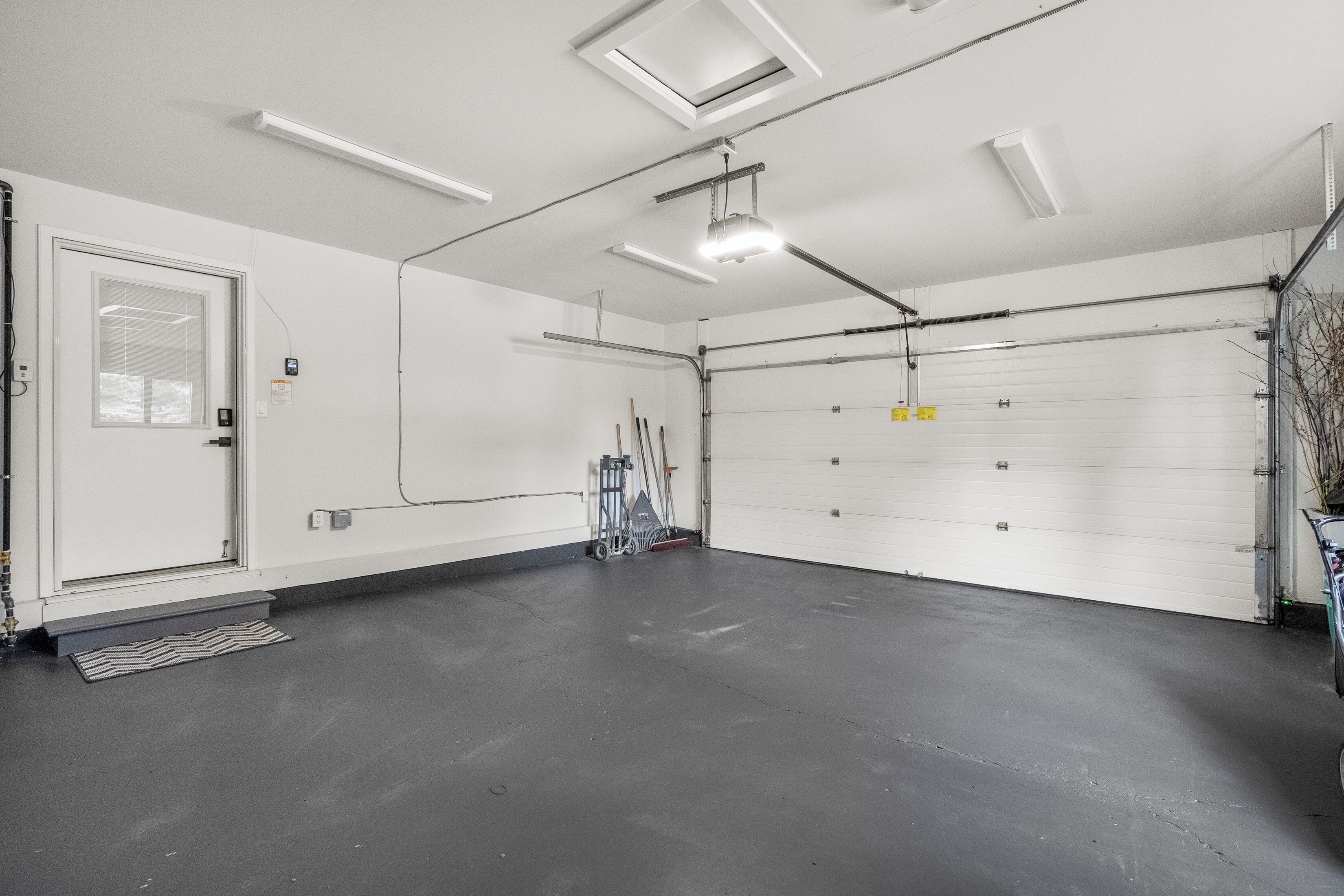 Uma garagem ampla e bem iluminada, com interior limpo e branco, uma porta de garagem grande e uma entrada com um pequeno degrau.