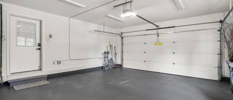 Un garage spacieux et bien éclairé, avec un intérieur propre et aux murs blancs, une grande porte de garage et une porte d’entrée avec un petit seuil.