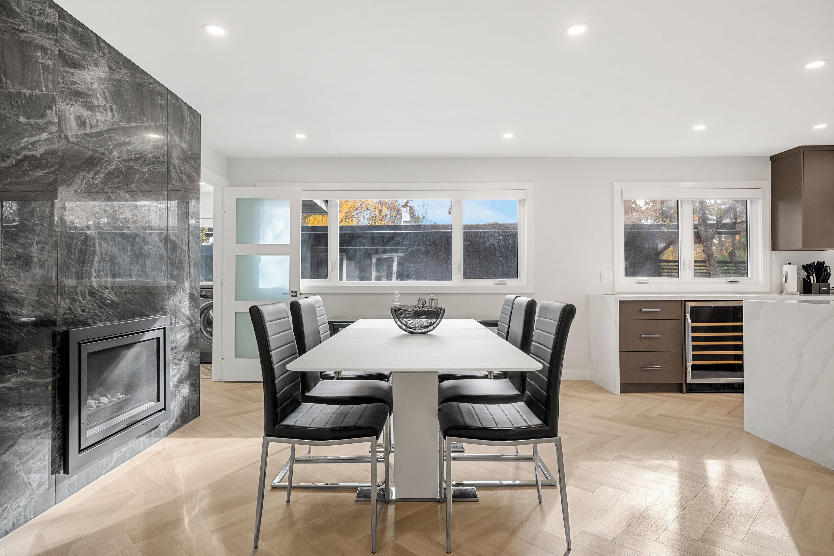 A modern kitchen with a marble backsplash, a built-in stove, and a dining area with a white table and black chairs.